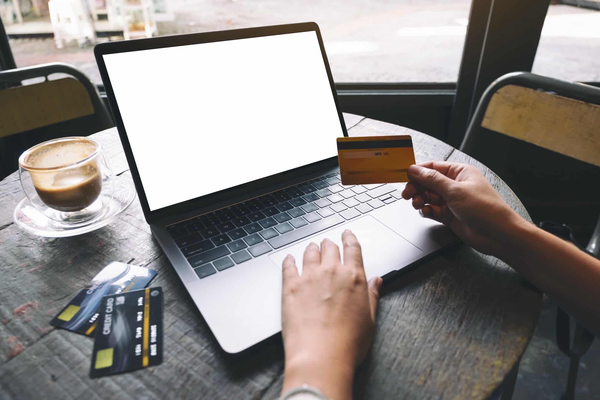 A woman holding credit card while using and typing on laptop with blank white screen