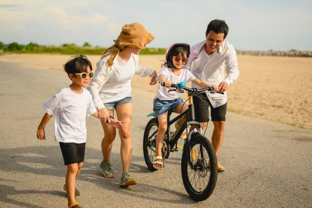 Happy family with outdoor activities riding bicycle together on beach