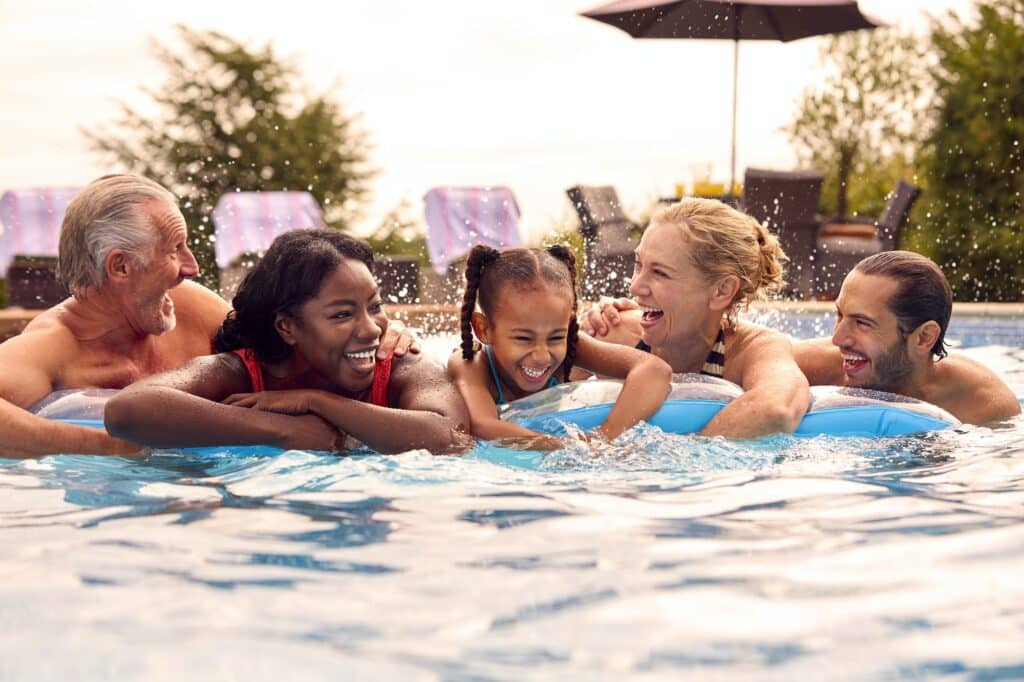 Smiling Multi-Generation Family On Summer Holiday Relaxing In Swimming Pool On Airbed