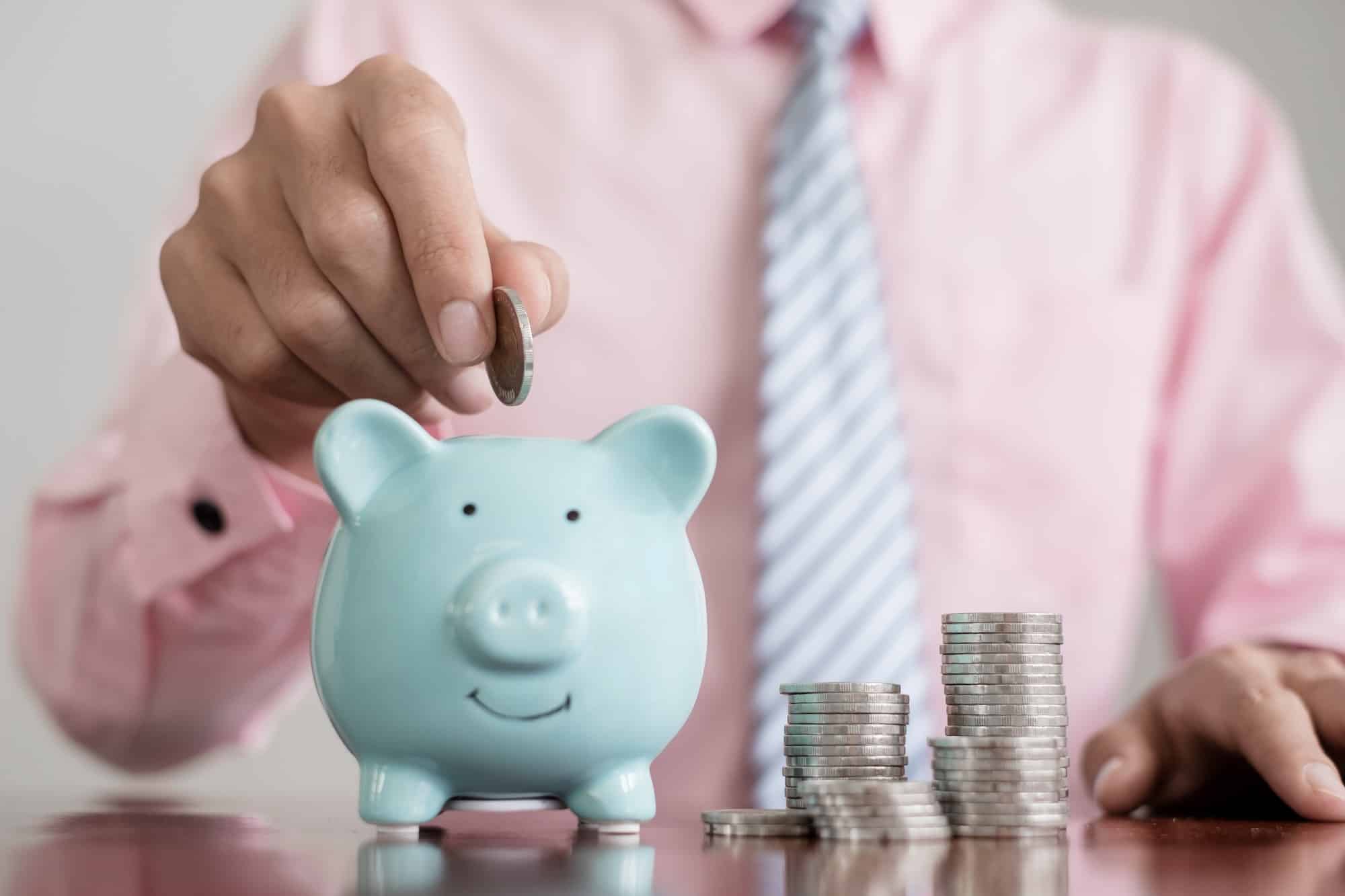 The hand of a businessman puts coins in a piggy bank, saves money with coins, steps into