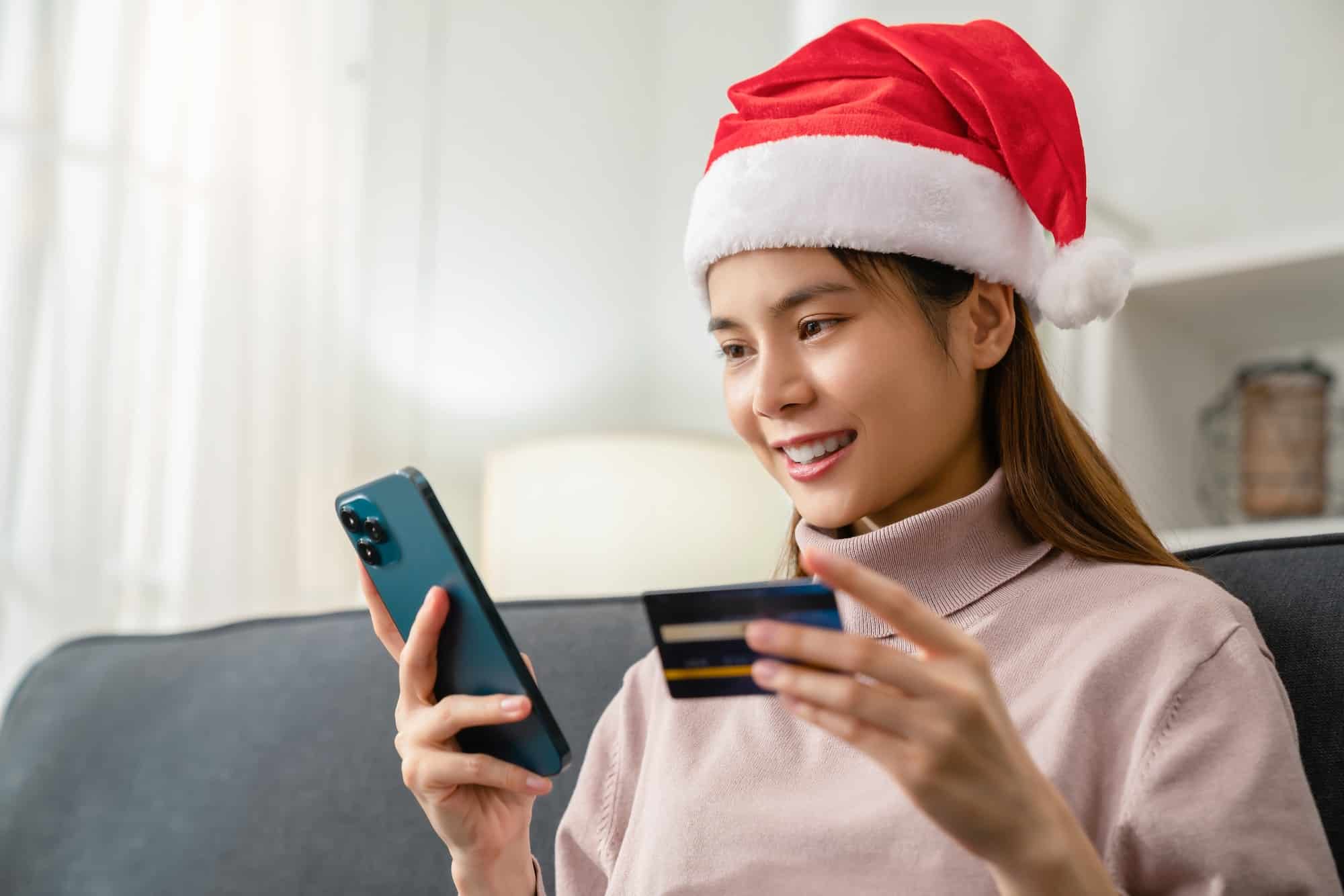 woman wearing red hat holding credit card and using smartphone for shopping online with payment.