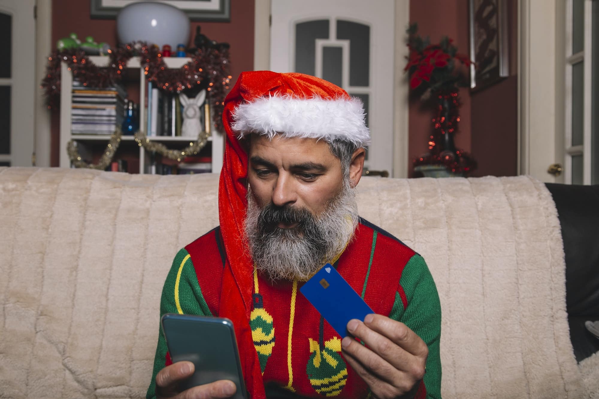 Man with christmas hat looks at the smartphone holding a credit card for online shopping. New year